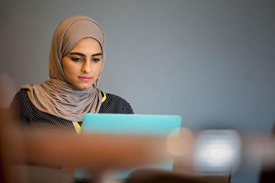 Photo of a Chatham University student in a hijab working at a computer in Cafe Rachel